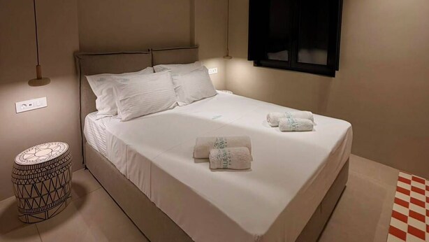 Un dormitorio moderno con una cama, ventilador de techo, televisor montado en la pared y una mesita de noche estampada.