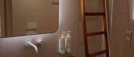 A bathroom with a modern sink, a mirror, a wooden ladder, and toiletries on a shelf.
