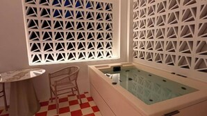 Un baño con piso de baldosas a cuadros, una bañera, un ventanal con diseño geométrico y una silla.