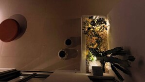 Un área de estar al aire libre con un diseño moderno, una escultura de cactus, una mesita y una pared decorativa con plantas.