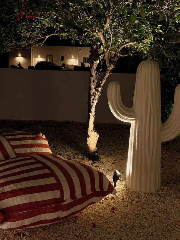A cactus sculpture, a striped pillow, and a tree with a lit base in a nighttime outdoor setting.