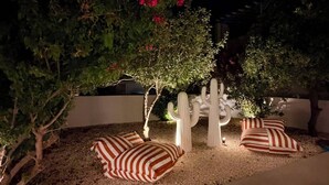 Un área de estar al aire libre con una escultura de cactus, un árbol con flores rojas y un banco con textura.