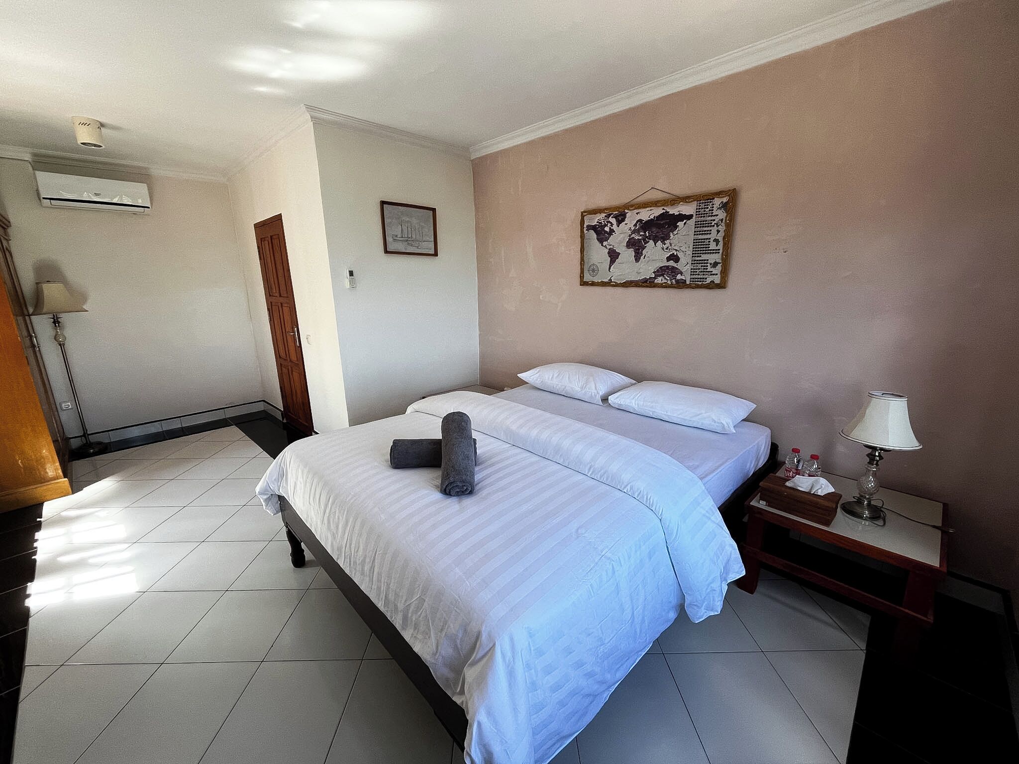 Una habitación de hotel con cama, mesita de noche, lámpara, mapa en la pared y puerta.