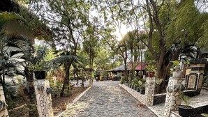 A stone pathway leading through a garden with trees and potted plants. - Mangga Lodge (Bira)