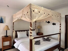 Una cama con dosel sobre pilares de madera y ropa de cama blanca, dos mesitas de noche con lámparas y decoraciones de peces colgadas en la pared.