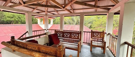Un espacio de estar al aire libre cubierto con bancos de madera y barandillas, rodeado por una estructura de techo rojo.