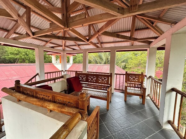 A covered outdoor seating area with wooden benches and railings, surrounded by a red-roofed structure.