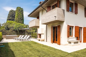 A modern two-story house with a balcony, a patio with lounge chairs, and a pool.