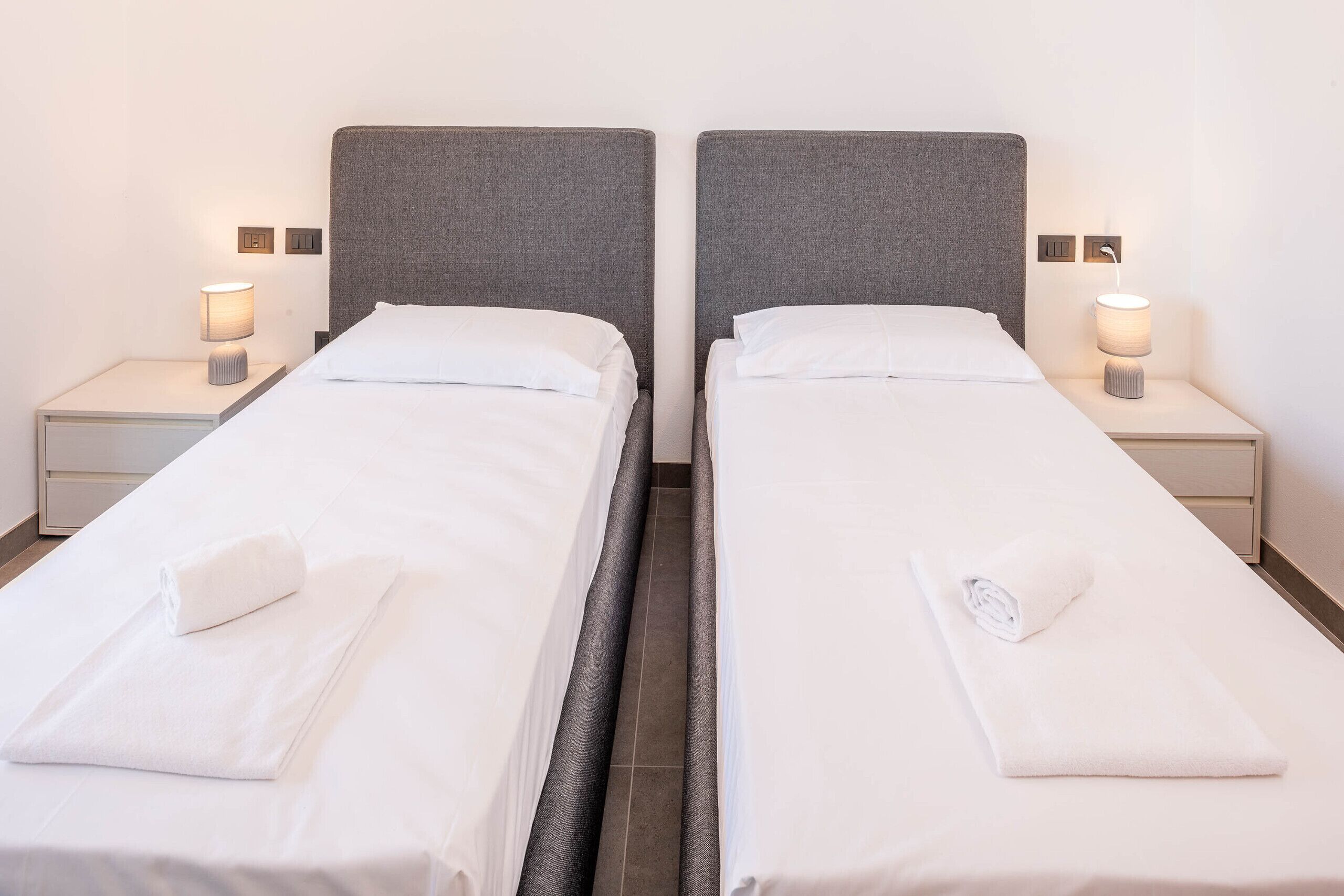 Una camera d'albergo con due letti singoli, ognuno con testiera, comodini e lampade.