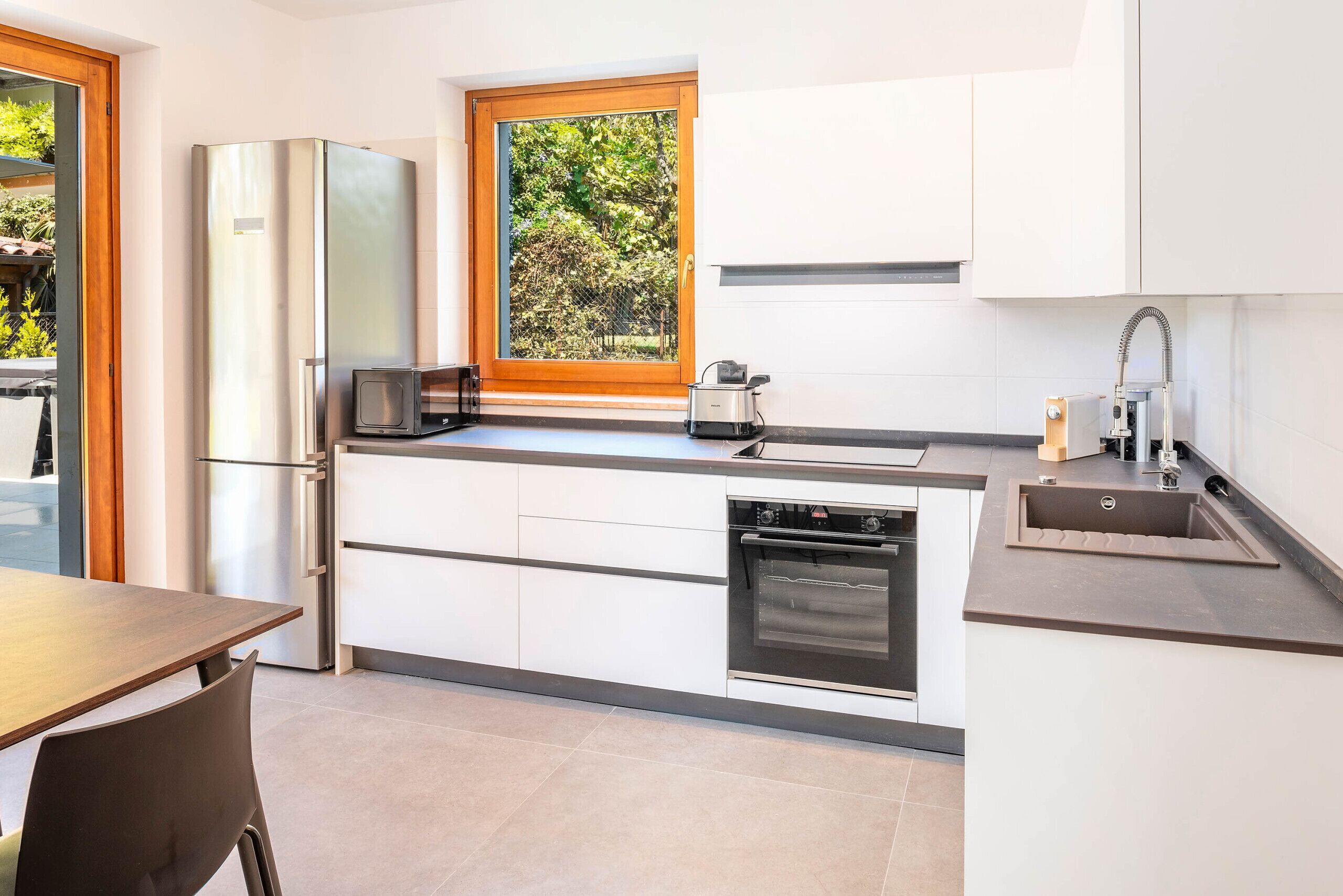 A modern kitchen with a built-in oven, microwave, and a window with a view of greenery.