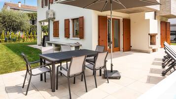 Une terrasse avec une table et des chaises, un parasol et un escalier menant à un balcon.