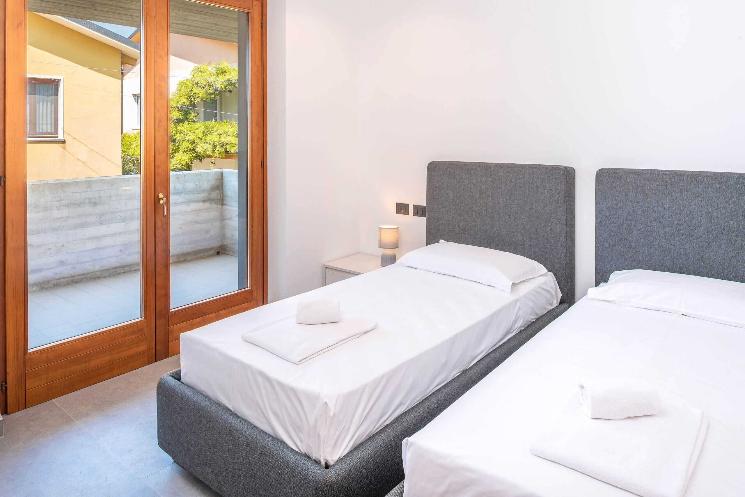 Ein Hotelzimmer mit zwei Betten, einer Schiebetür zu einem Außenbereich und einem kleinen Nachttisch mit einer Lampe.