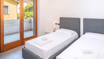 Ein Hotelzimmer mit zwei Betten, einer Schiebetür zu einem Außenbereich und einem kleinen Nachttisch mit einer Lampe.
