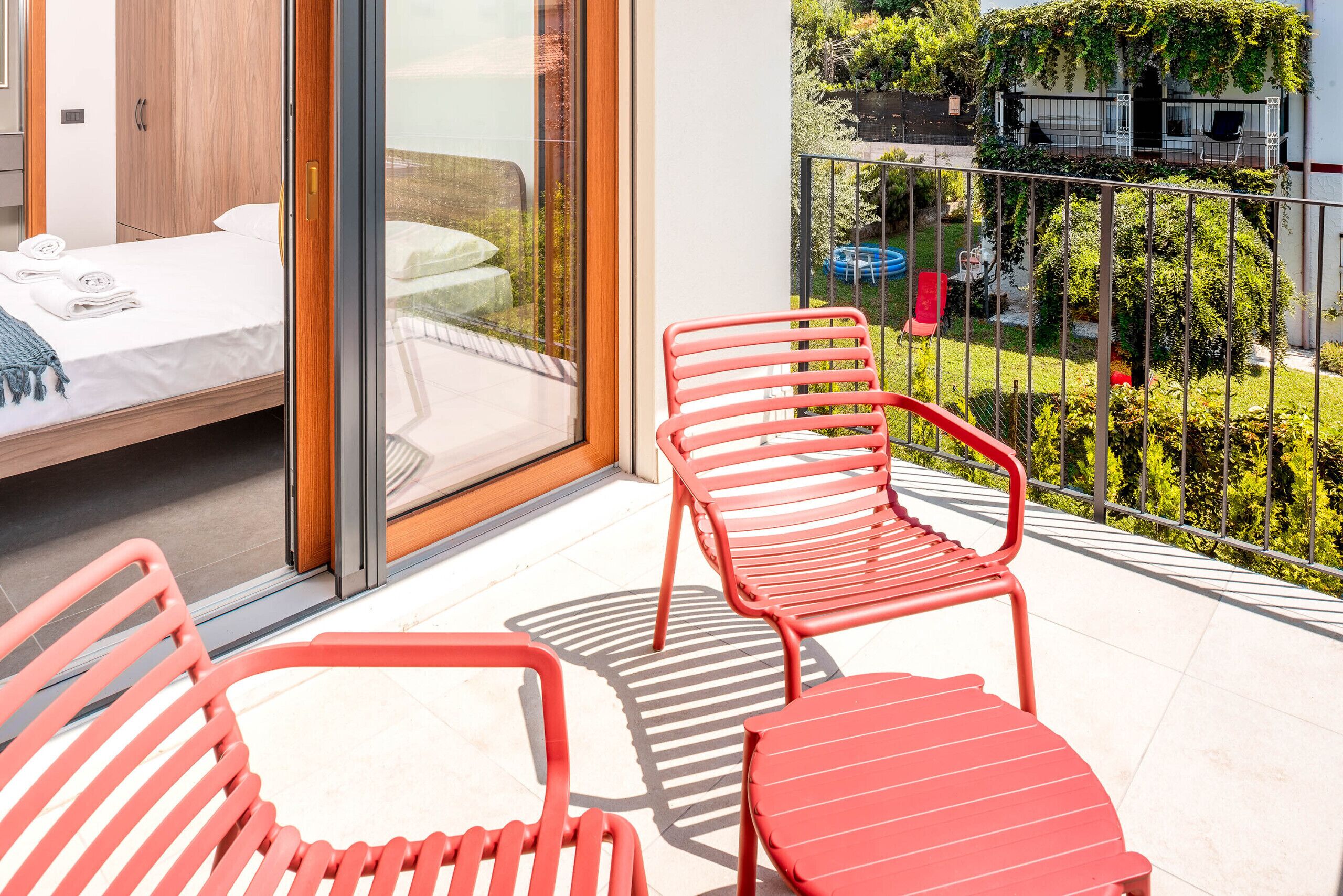 Ein Balkon mit einem Bett, einem roten Stuhl und Blick auf einen Garten.