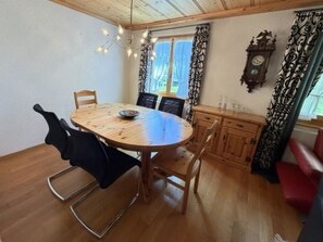 Un comedor con una mesa redonda de madera, cuatro sillas, una araña y un aparador con un reloj.
