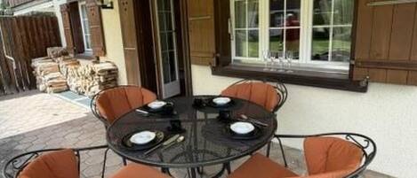 An outdoor patio with a round table and four chairs, a window with shutters, and a door.