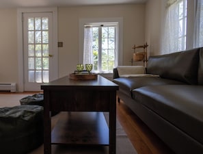 Ein Wohnzimmer mit einem dunkelbraunen Tisch, einem Ledersofa und zwei mit Vorhängen versehenen Fenstern.