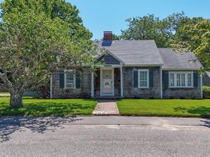 A two-story stone house with a front porch, a chimney, and a well-maintained lawn. - Lewis Bay Celtic Cottage is a restored antique home steps away from Lewis Bay (Yarmouth)