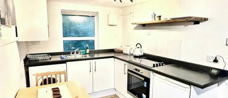 A compact kitchen with white cabinets, a wooden dining table, and a built-in oven.