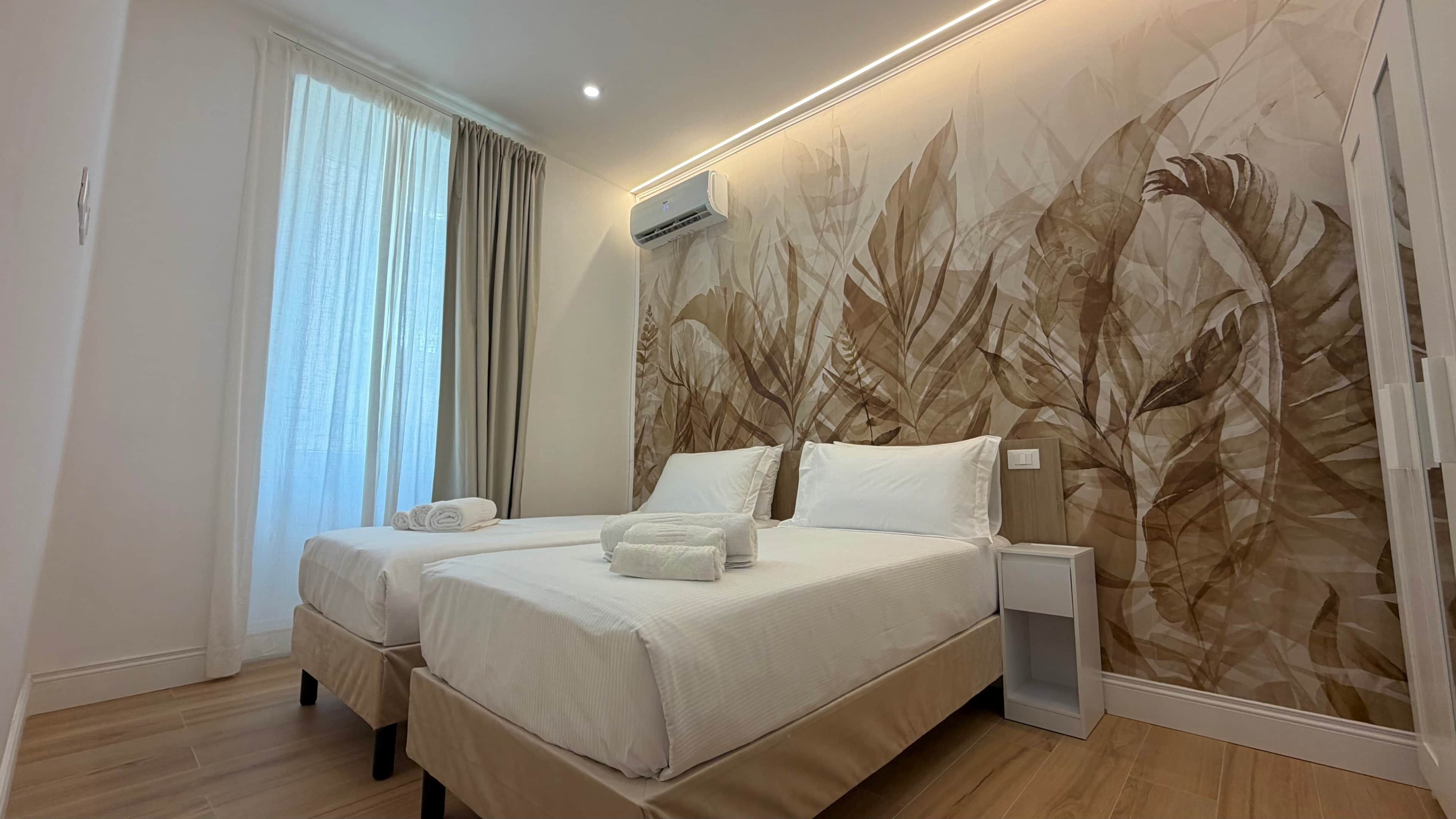 Hotelkamer met een groot bed, twee nachtkastjes, een wandairconditioner en een raam met gordijnen.