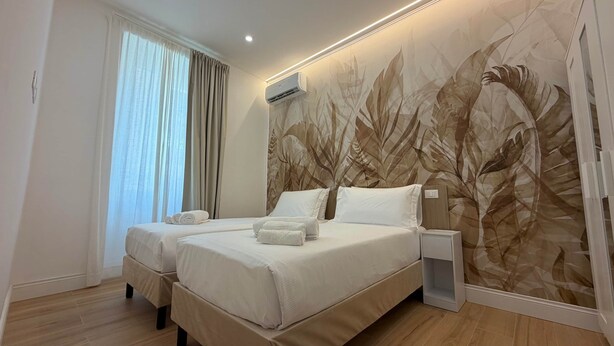 A hotel room with a large bed, two bedside tables, a wall-mounted air conditioner, and a window with curtains. - Apollo&Co.House,Perfect Stay before/after cruise,2/4 people (Civitavecchia)
