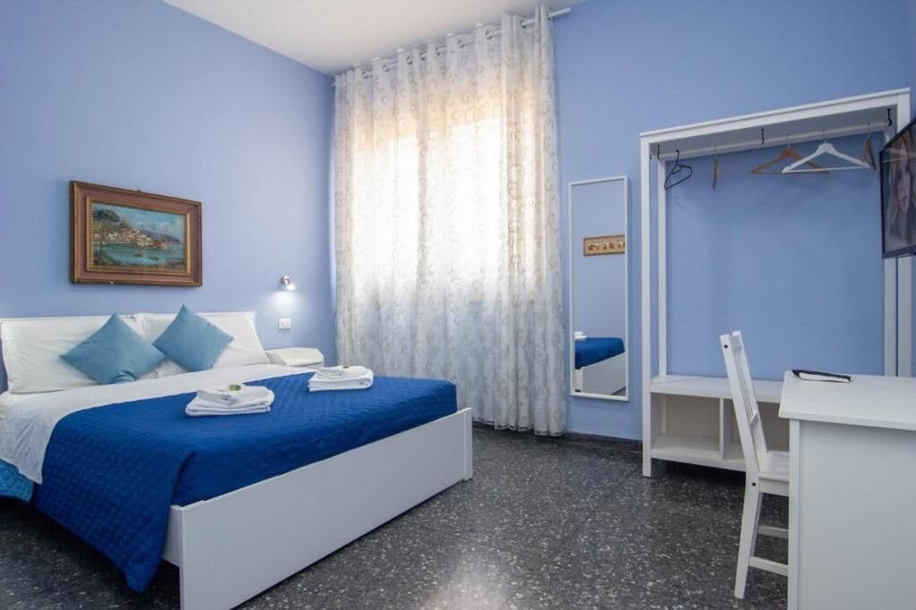 Une chambre à coucher avec un lit, un bureau, une chaise, un miroir et un tableau accroché au mur.
