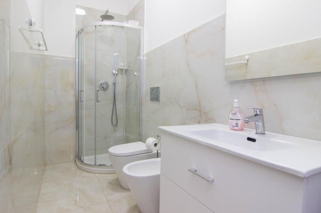 A modern bathroom with a glass-enclosed shower, two toilets, a white sink, and a mirror above the sink.