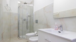 Un baño moderno con ducha de vidrio, dos inodoros, un lavabo blanco y un espejo sobre él.