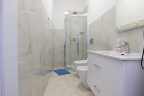 Ein modernes Badezimmer mit einer gläsernen Duschkabine, einer Toilette und einem Waschtisch mit Spiegel.