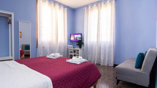 Una habitación de hotel con cama, una silla, un televisor y cortinas.