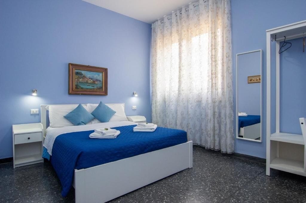 A bedroom with a bed, nightstands, a mirror, and a painting on the wall.