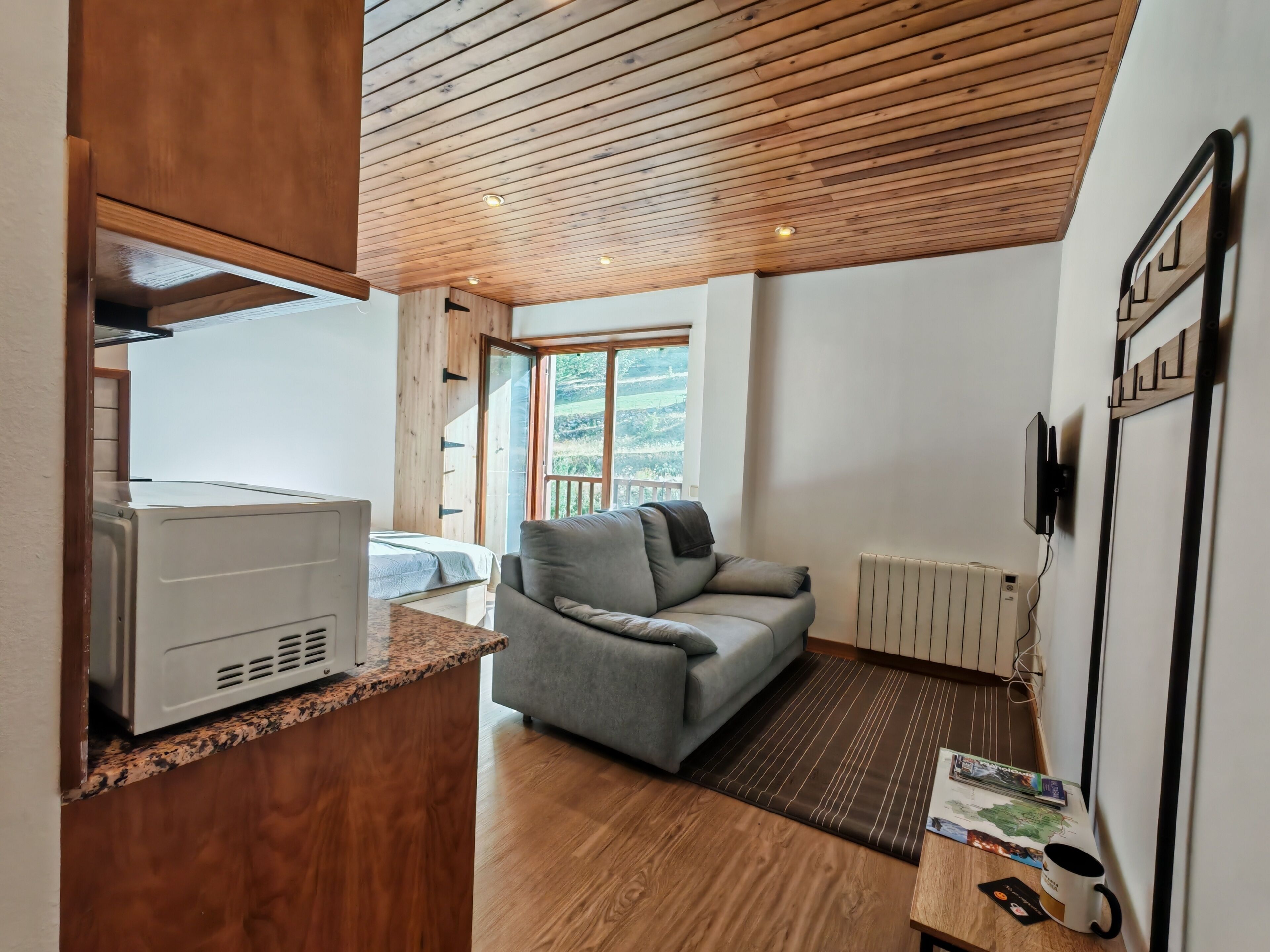 En modern inredning med ett träpanelat tak, en grå soffa, ett element och en tv som är monterad på väggen.