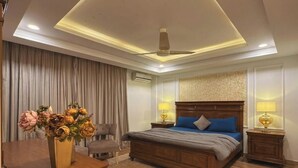Quarto de hotel com uma cama grande, luminárias de cabeceira, um ventilador de teto e um vaso de flores.