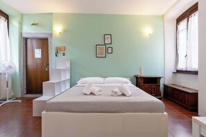 Ein Hotelzimmer mit Bett, Nachttisch, Ventilator, Holzschrank und einem Fenster mit Vorhängen.