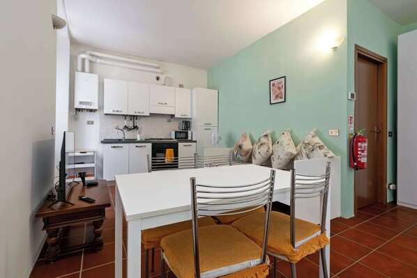 A compact kitchen with white cabinets, a microwave, and a gas stove. There is a dining table with chairs and a small wooden table with a remote control.