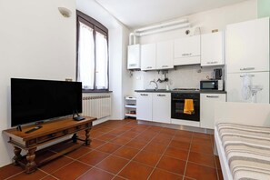 A compact kitchen with white cabinets, a built-in oven, a microwave, and a window with curtains.