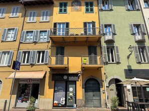 Ein mehrgeschossiges Gebäude mit einem Laden im Erdgeschoss, einem sichtbaren Eingang und einem Balkon mit Metallgeländer.