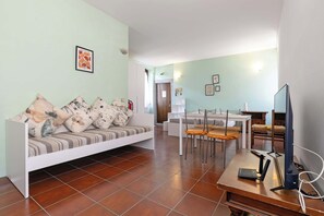 A living room with a sofa, a dining table with chairs, a television, and a fireplace.