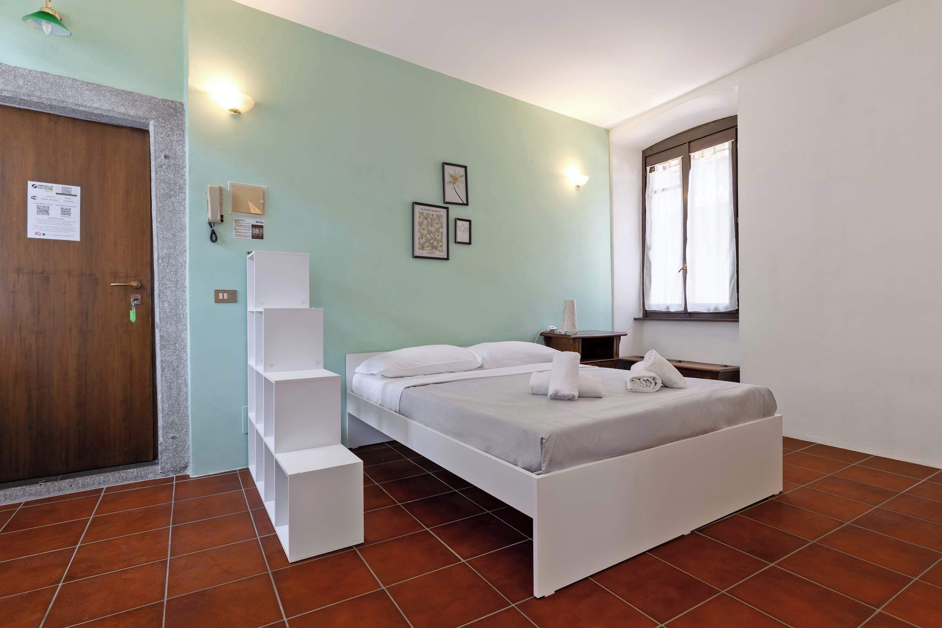 Une chambre d’hôtel avec un lit, un bureau, une chaise, une armoire, une porte et une fenêtre.