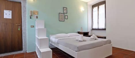 A hotel room with a bed, a desk, a chair, a wardrobe, a door, and a window.