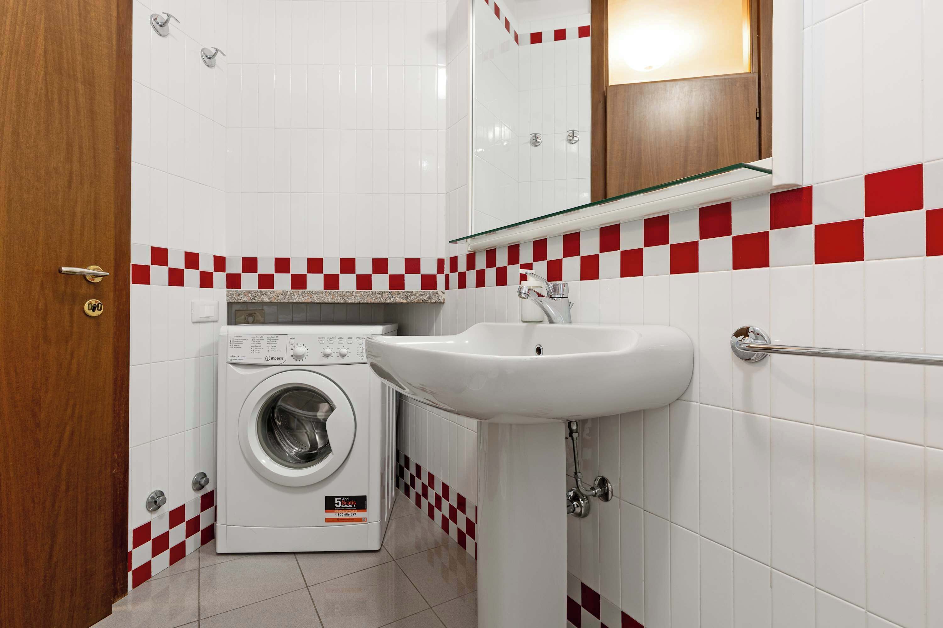 Ein kleines Badezimmer mit Waschmaschine, Waschbecken und Spiegel.