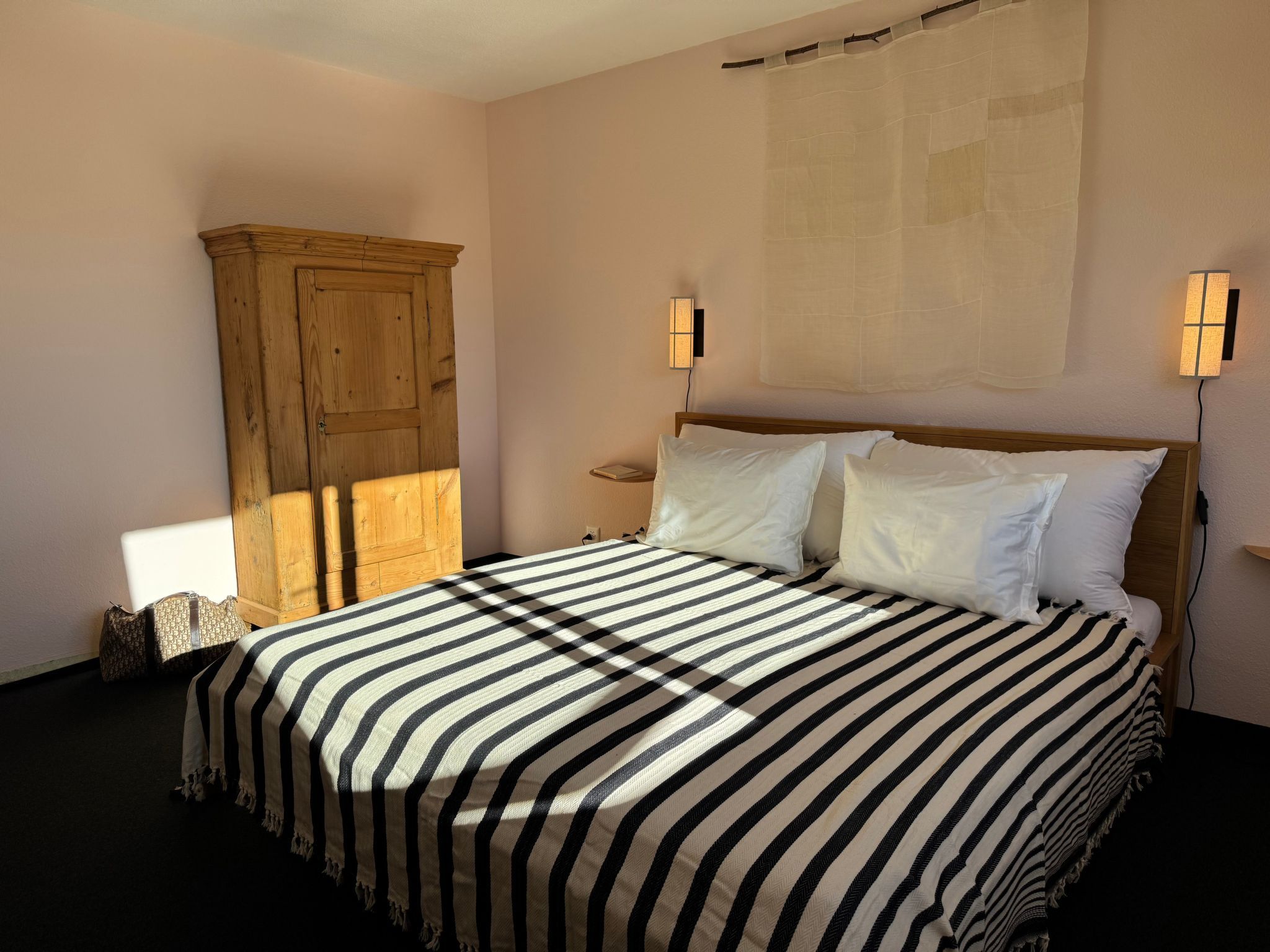 Un dormitorio con una cama, un armario de madera y dos luces fijadas a la pared.