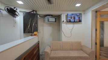 A room with a sofa, a television mounted on the wall, a fan, and a wooden cabinet.