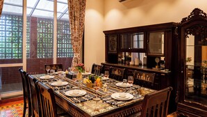 A dining room with a long table set for six, surrounded by chairs, with a large window and a decorative cabinet.