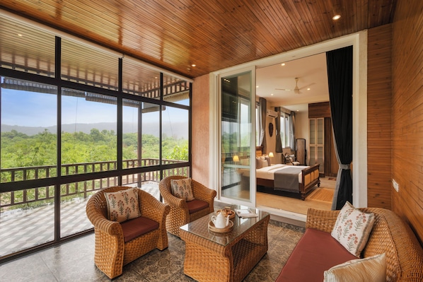 A spacious balcony with wicker furniture, a glass door leading to a bedroom, and a view of a lush landscape.