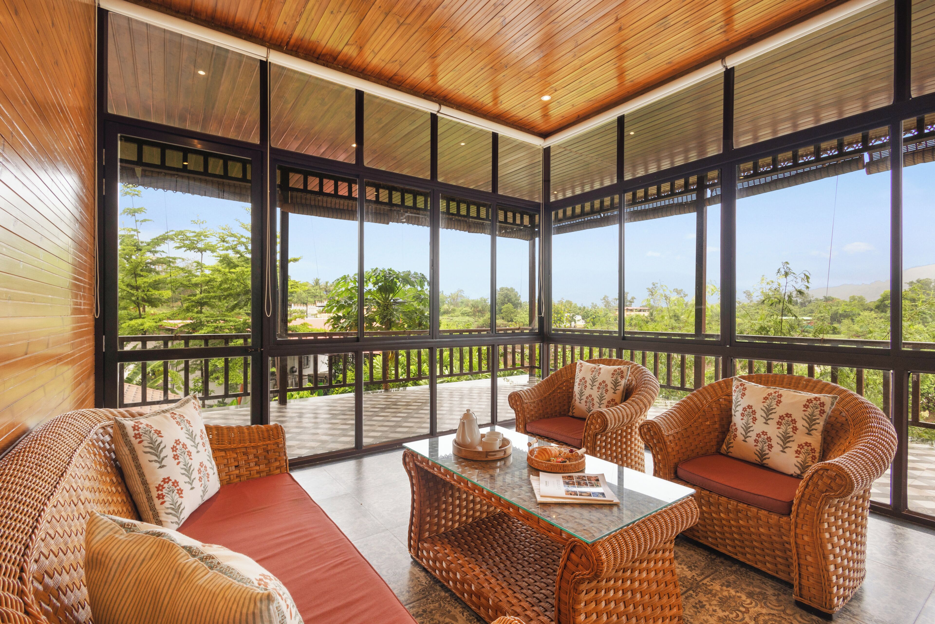 A spacious balcony with wicker furniture and a glass coffee table, overlooking a lush landscape.