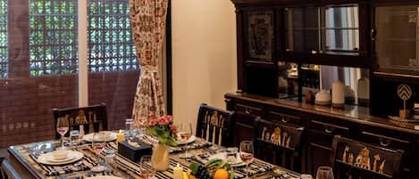 A dining room with a long table set for six, surrounded by chairs, with a ceiling fan above and an air conditioning unit on the wall.
