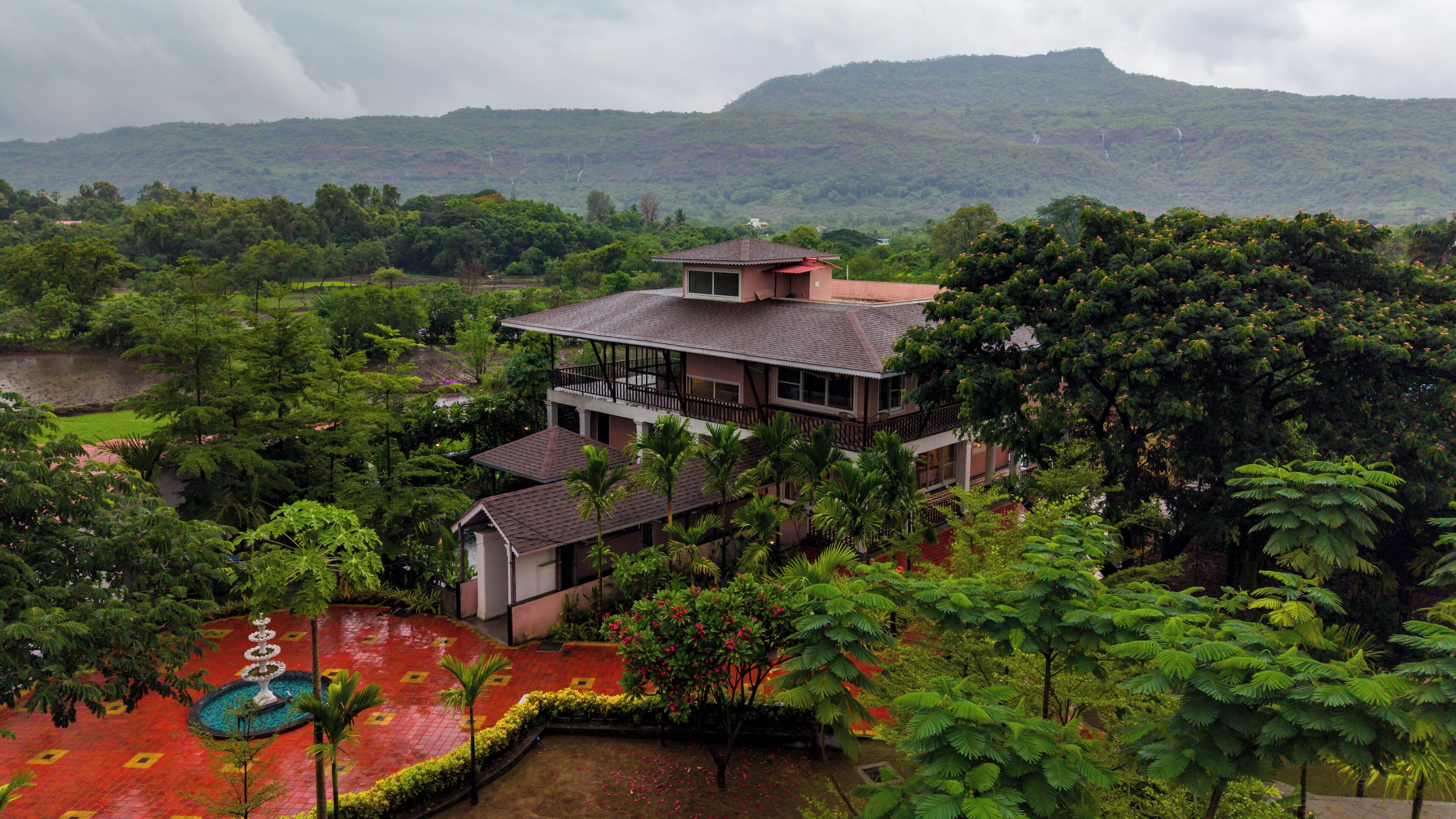 A two-story building with a balcony, surrounded by lush greenery and a view of a hill.