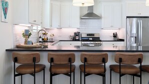 Een moderne keuken met witte kasten, een centraal eiland met barkrukken, roestvrijstalen apparatuur en een hanglamp.