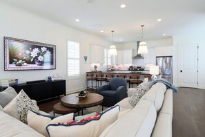 Un salon moderne avec un canapé, une table basse et un coin repas comprenant des chaises, et une cuisine en arrière-plan.